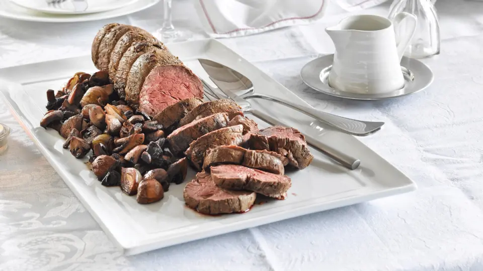 cooked whole roast beef on white plate served with shallots